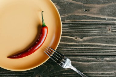 Fork on plate with red pepper on wooden table clipart