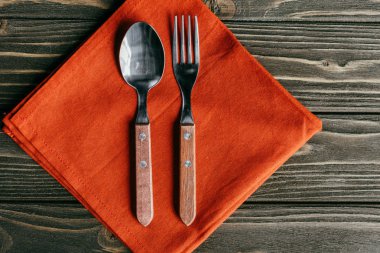 Silverware set with orange napkin on wooden table clipart