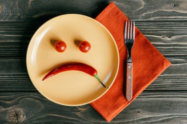 Biber ve portakal peçete üzerinde çatalı ile plaka üzerinde domates üzgün smiley yapılmış