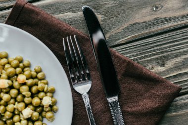 Fork and knife by plate with peas on textile napkin clipart