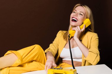 sarı vintage telefonla konuşurken ve kahverengi üzerine gülen neşeli sarışın kız