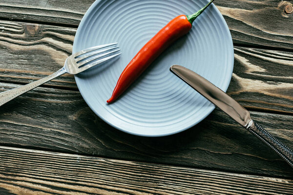 Fork and knife on plate with red pepper on wooden table