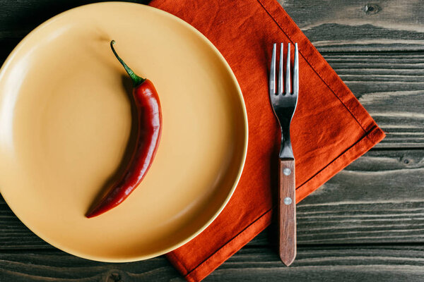 Yellow plate with spicy pepper on wooden table on textile napkin