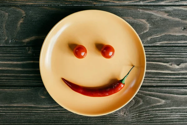 木桌上用胡椒和西红柿做的微笑盘子 — 图库照片