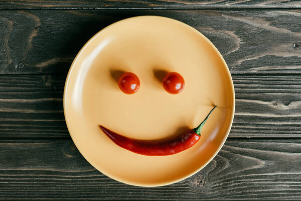 Plate with smile made of pepper and tomatoes on wooden table