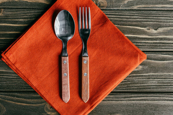 Silverware set with orange napkin on wooden table