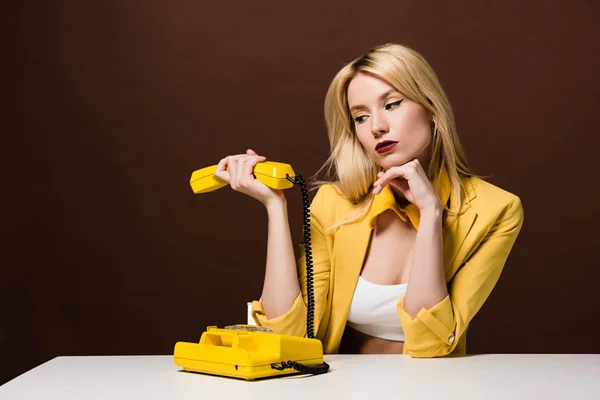 Reflexiva Chica Rubia Sosteniendo Auricular Amarillo Mientras Está Sentado Marrón — Foto de Stock