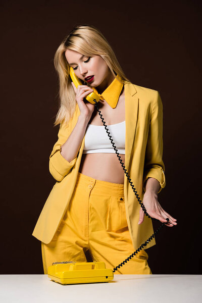 стильная блондинка в желтой одежде говорит по ротационному телефону на коричневый

