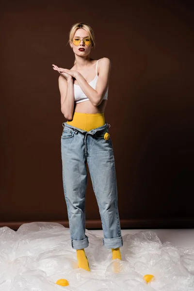 黄色のサングラス立っているとスタジオでカメラ目線で美しいスタイリッシュな若いブロンドの女性  — 無料ストックフォト