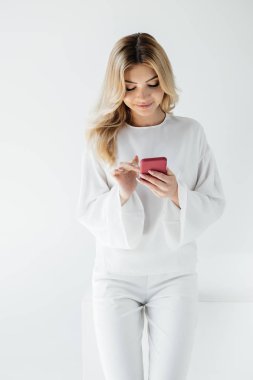 gri izole smartphone kullanarak beyaz giyim gülümseyen sarışın kadın