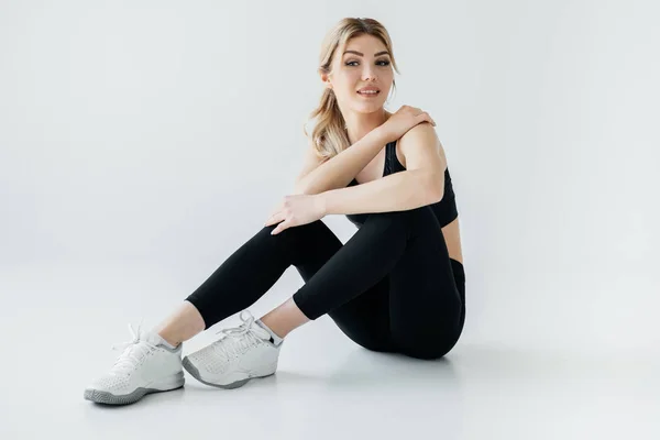 Lachende Sportvrouw Zwarte Sportkleding Zittend Vloer Geïsoleerd Grijs — Stockfoto