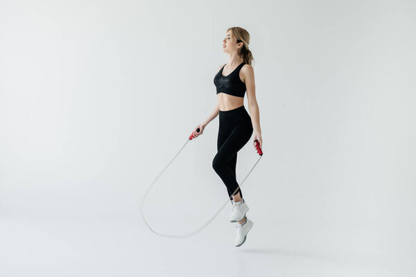 young sportive woman exercising with skipping rope isolated on grey