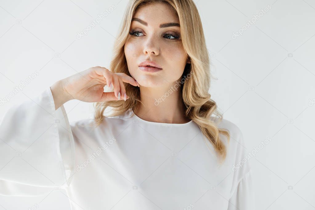 portrait of pensive blond woman in white clothing posing on white backdrop