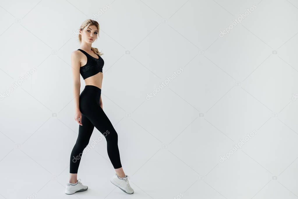 side view of young blond sportswoman in black sportswear posing isolated on grey