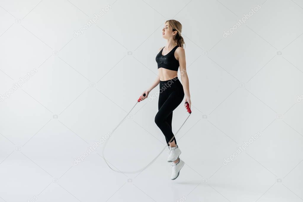 young sportive woman exercising with skipping rope isolated on grey