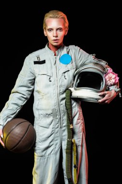 attractive female astronaut in spacesuit holding basketball and helmet with flower, isolated on black clipart