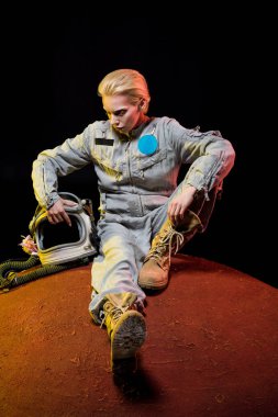 gezegen üzerinde oturan kask ile uzay giysisi içinde güzel astronot