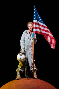 attractive female astronaut in spacesuit holding helmet and american flag on planet  clipart