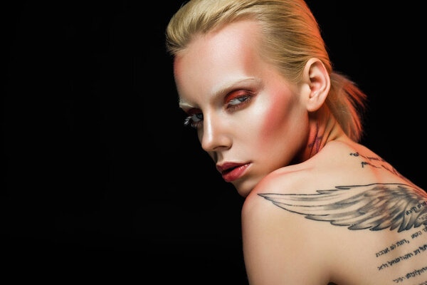 sensual naked woman with tattooed wings on back, isolated on black