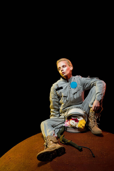 beautiful astronaut in spacesuit with flowers in helmet sitting on planet 