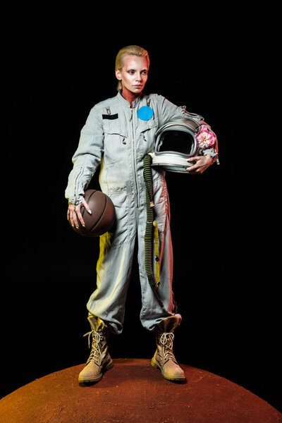 cosmonaut in spacesuit holding basketball ball and helmet with flower while standing on red planet 