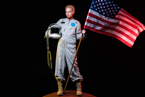 spacewoman in spacesuit holding helmet and american flag on mars