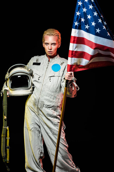 beautiful female cosmonaut in spacesuit holding helmet and usa flag, isolated on black