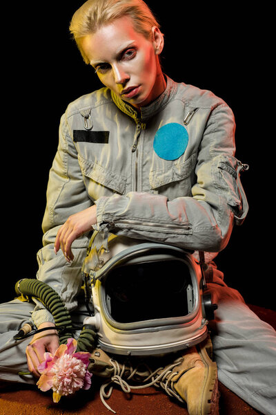 attractive young astronaut in spacesuit with helmet and peony sitting on planet