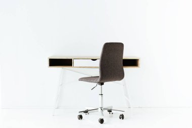 stylish empty work table and wheeled chair in front of white wall clipart