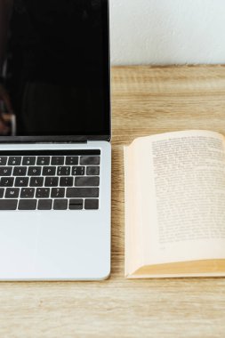 ahşap masa üzerinde açık kitap ile dizüstü yakın çekim vurdu