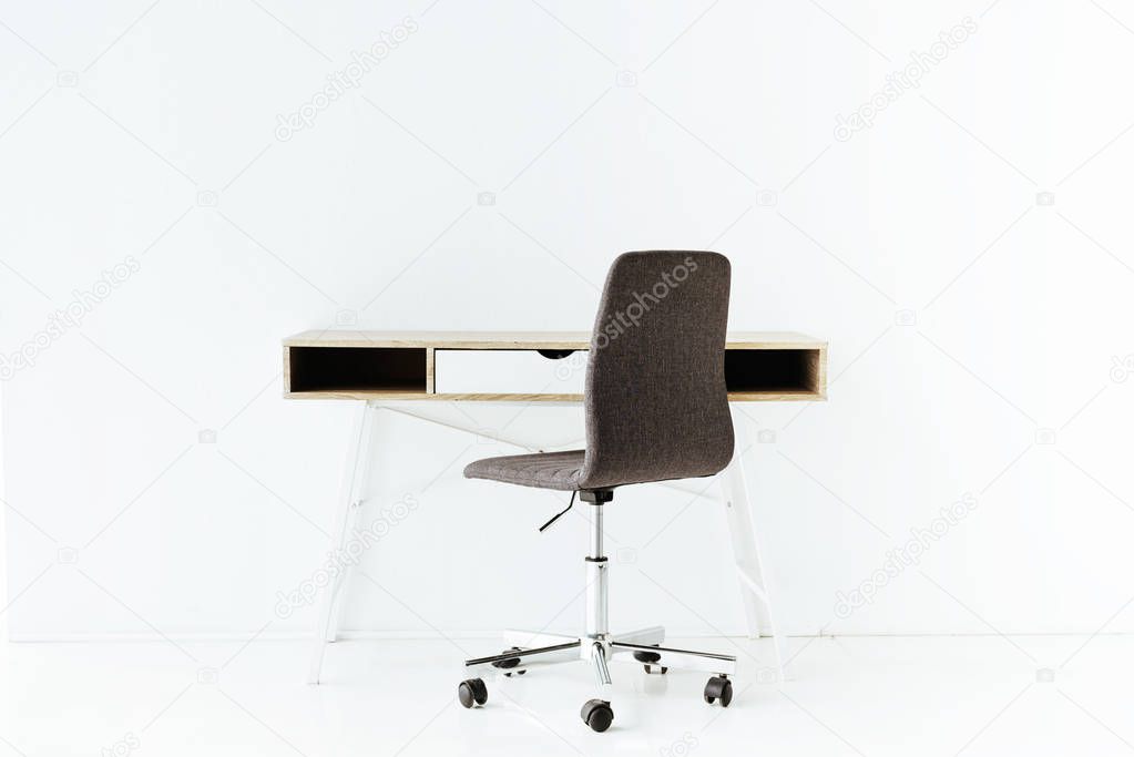 stylish empty work table and wheeled chair in front of white wall