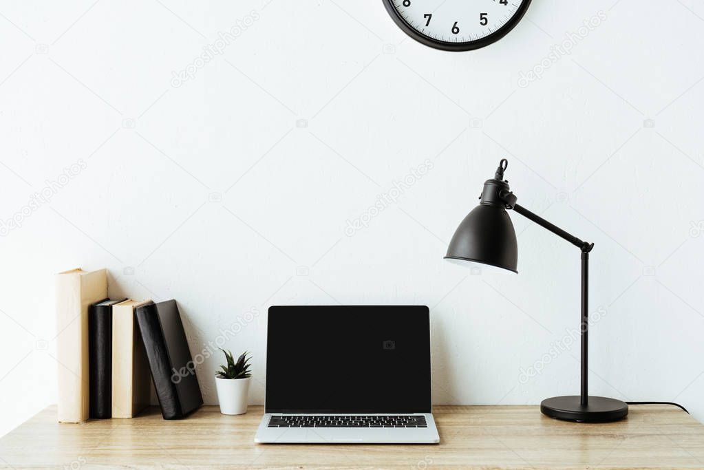 laptop with blank screen on work desk in front of white wall