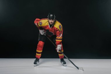 serious sportsman playing ice hockey and looking at camera on black  clipart