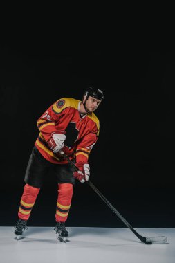 full length view of handsome young sportsman in protective sportswear playing hockey on black clipart