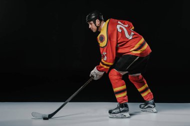 Hokey oynamak ve uzak siyah üzerinde seyir profesyonel genç buz hokeyi oyuncusu yan görünüm  