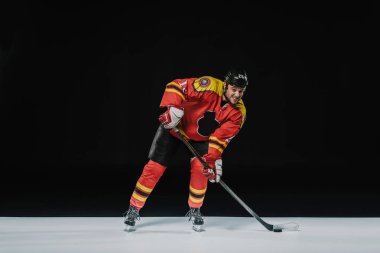 full length view of young professional sportsman playing ice hockey on black  clipart