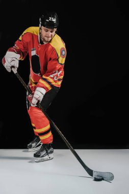 full length view of professional sportsman in skates playing hockey on black clipart