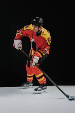 full length view of professional sportsman playing hockey and looking away on black clipart