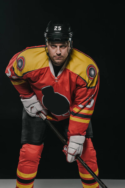 professional ice hockey player holding hockey stick and looking at camera on black 