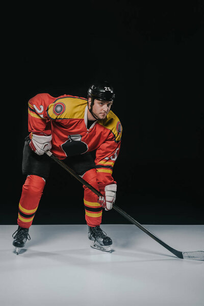 full length view of serious sportsman playing ice hockey and looking away on black 