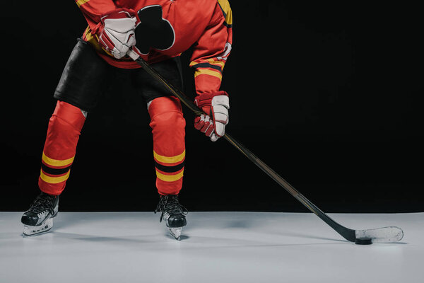 cropped shot of sportsman with hockey stick playing ice hockey on black