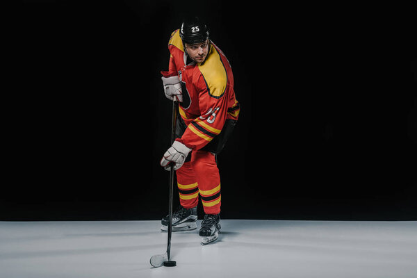 full length view of professional sportsman in skates playing ice hockey on black  