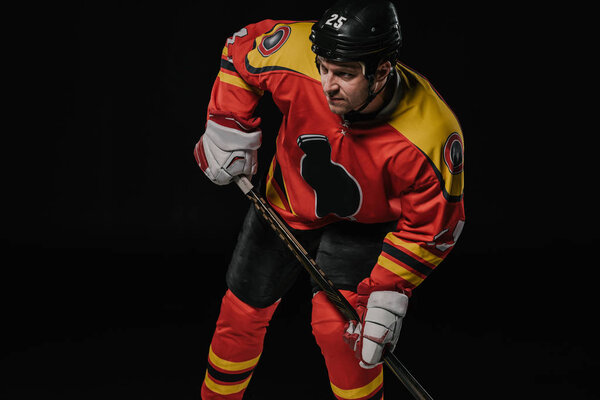 professional hockey player in protective sportswear holding hockey stick and looking away isolated on black
