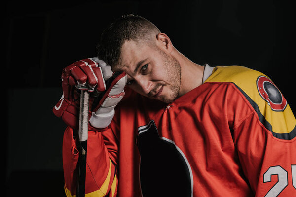 young hockey player leaning at hockey stick and looking at camera isolated on black
