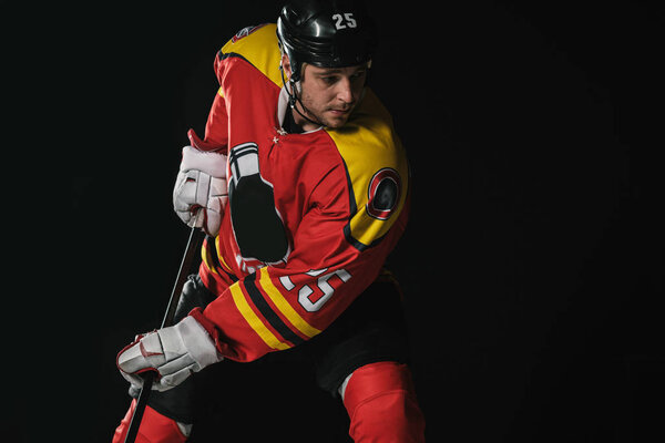 young hockey player in protective sportswear playing hockey isolated on black