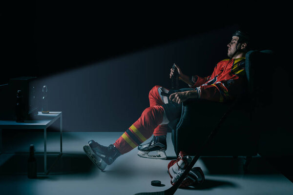 side view of young hockey player drinking beer and watching tv on black 