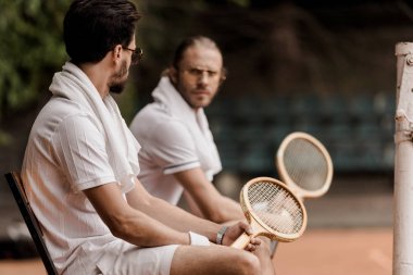 Tenis Kortu havlu ve raketleri ile sandalyelere oturan ciddi retro tarz tenis oyuncuları 