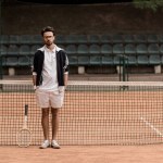 Guapo jugador de tenis de estilo retro de pie en la pista de tenis y mirando a la cámara