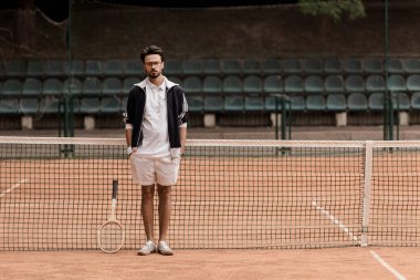 Tenis Kortu ayakta ve kameraya bakarak yakışıklı retro tarz tenis oyuncusu