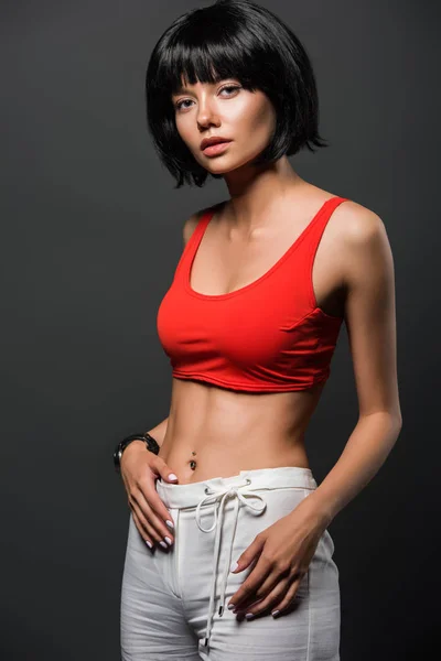 slim young woman in red crop top looking at camera isolated on grey